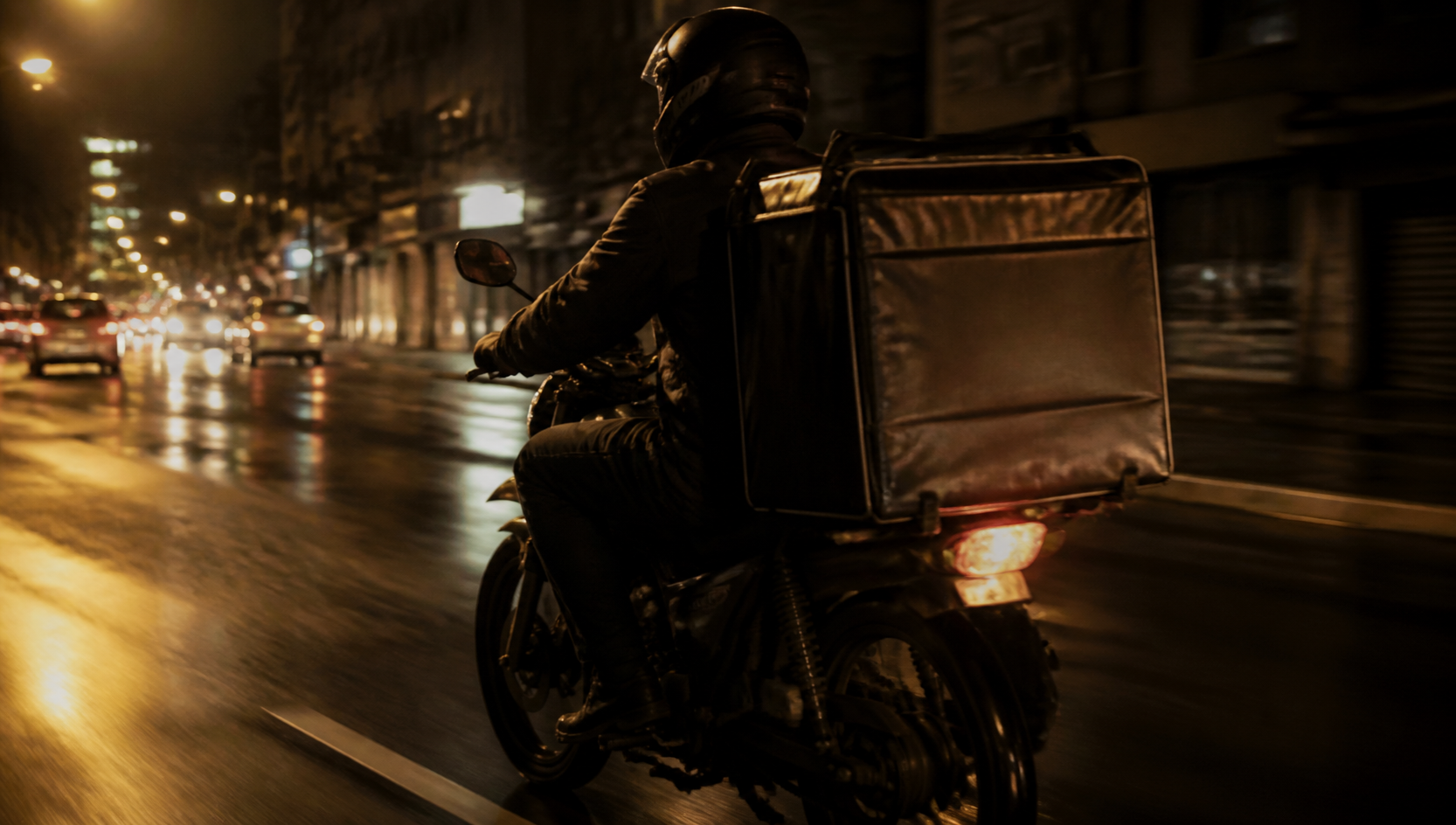 Motofretista pilotando em avenida urbana à noite